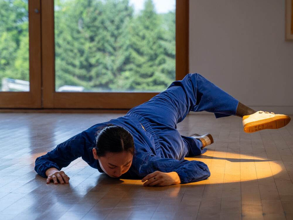A dancer in a blue velour jumpsuit performing in an art gallery
