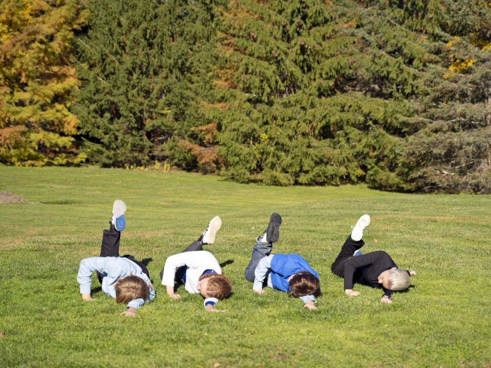 Four dancers lying in the grass with on knee bent and foot pointed skyward.