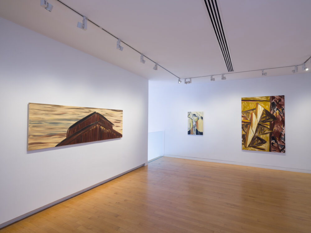 View of a corner of a gallery with a painting hung on each wall.