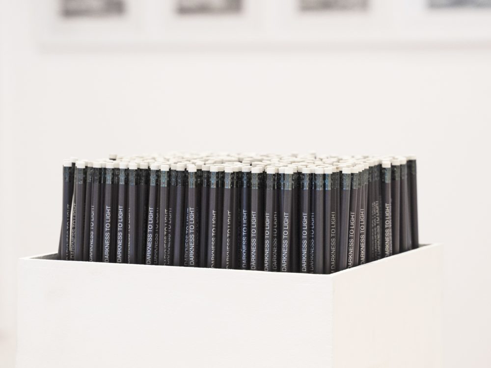 A white box filled with black pencils with white text standing up.