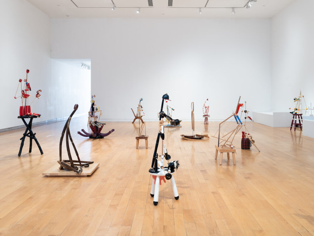 A side view of an installation of figurative sculptures filling a gallery space.