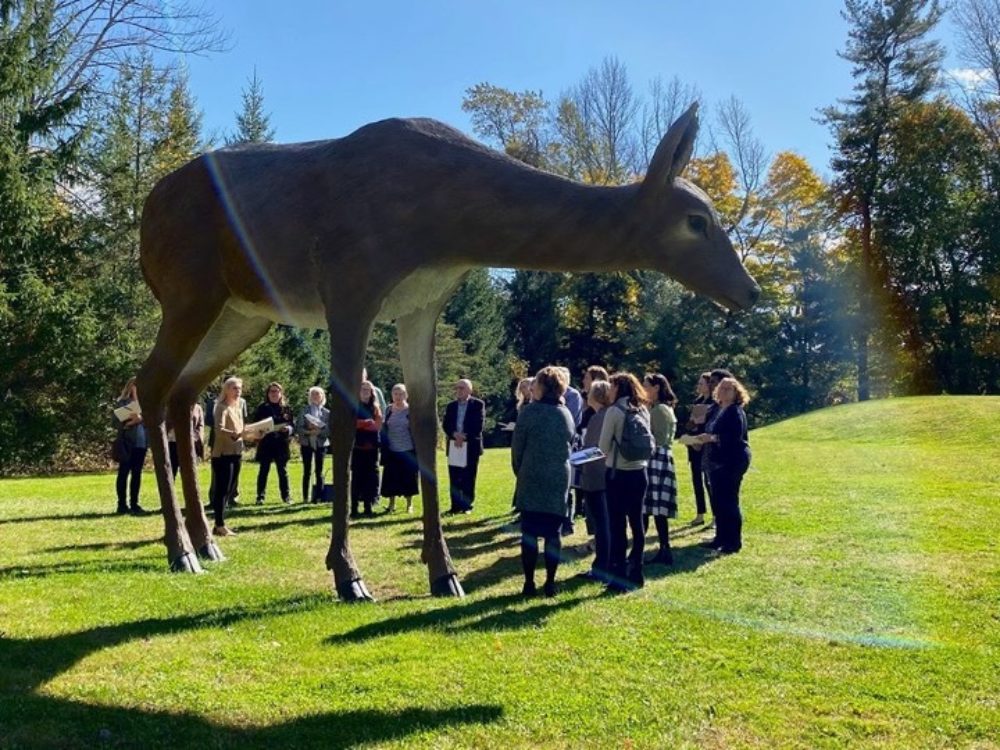 Group of people standing around a large scale sculpture of a white tailed deer in the Sculpture Garden.