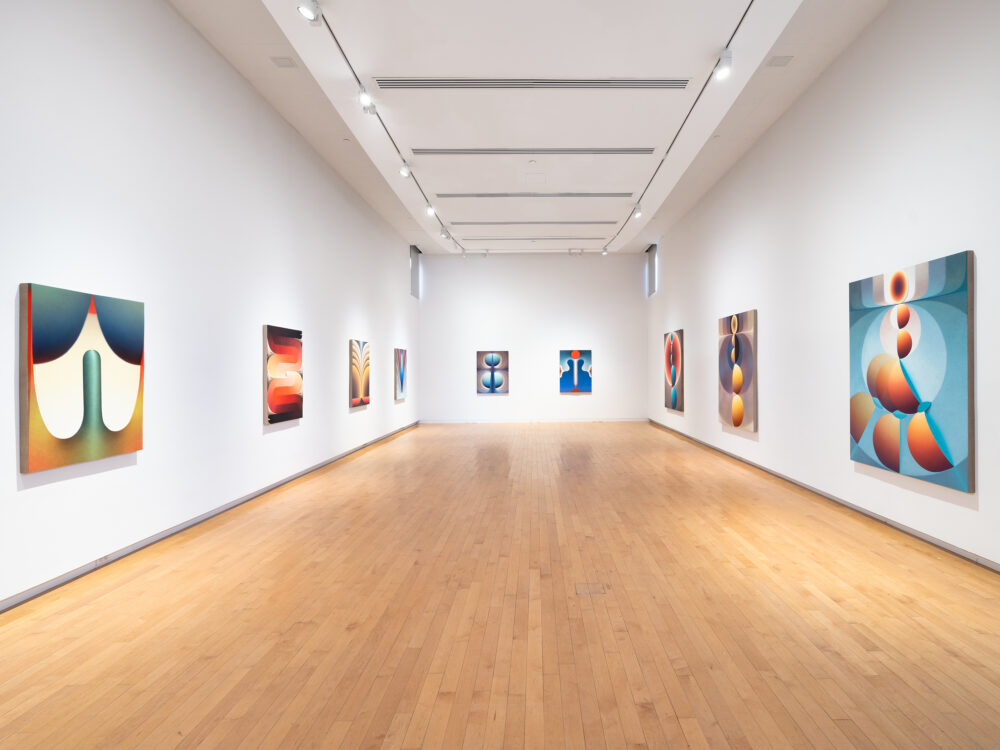Colorful paintings installed in a row on three walls of a gallery