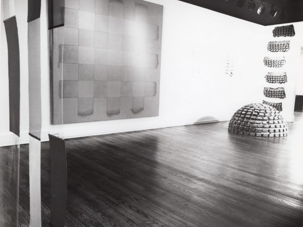 Black and white photograpy of a brick dome floor sculpture, a gridded painting, and a hanging textile sculpture.