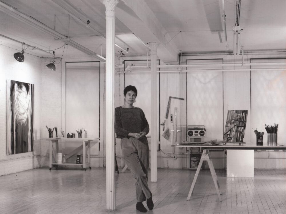 Black and white photo of a woman standing in a loft studio space.