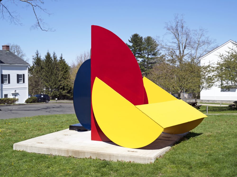 Outdoor abstract sculpture with three primary colored pieces on a lawn.