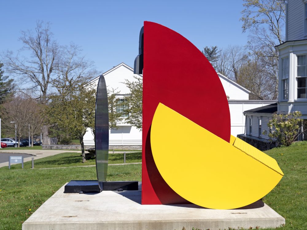 Abstract sculpture with three primary colored pieces on a lawn.