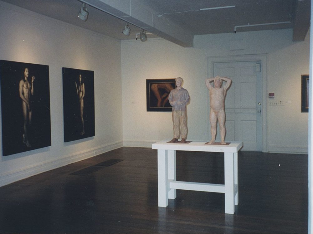 This is a view of one of the galleries from The Nude in Contemporary Art Exhibition. Two large photos are on display with two small figures in the center