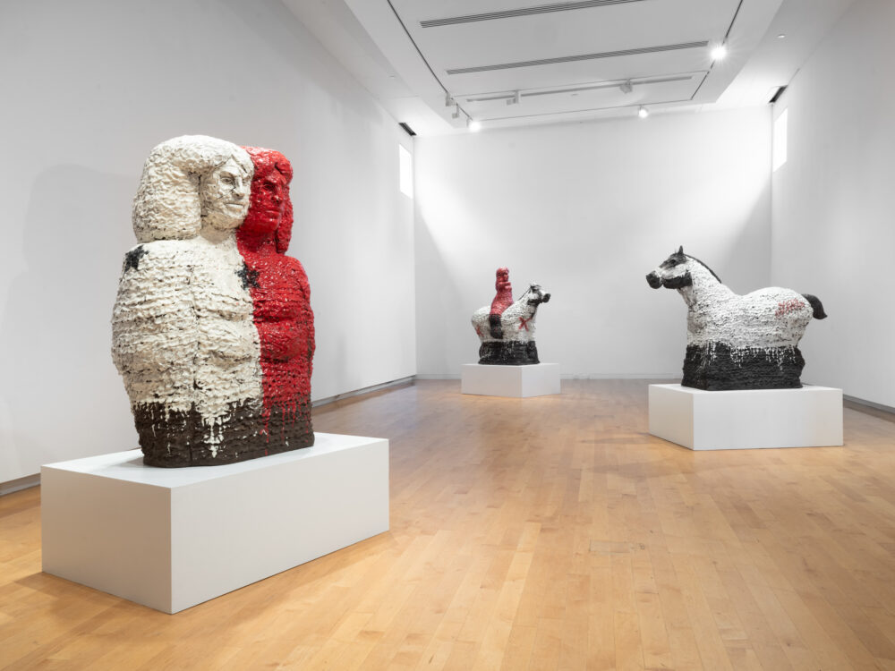 Installation view of a gallery with large scale ceramic sculptures on white pedestals.