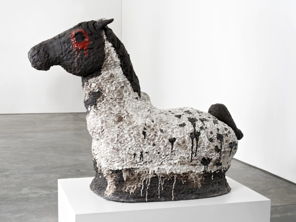 Ceramic sculpture of a horse with no legs on a plinth.