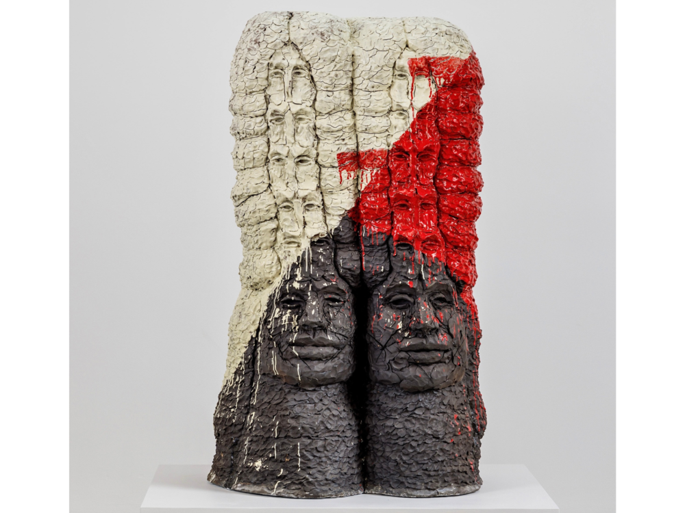 Ceramic work with two stacks of faces fused together in shades of white, red, and black.