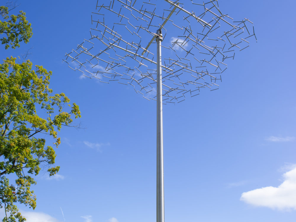 Close up image of kinetic sculpture set against the sky on top of a steel pole.