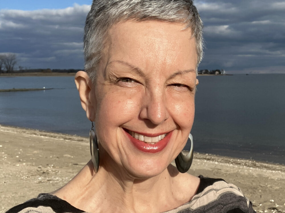 A smiling woman with short gray hair with the ocean in the background