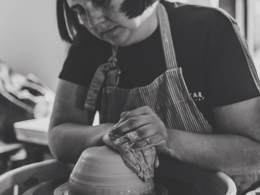 A woman centering clay on a potter's wheel.