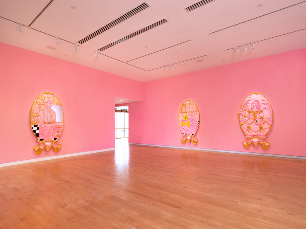 Pink walls with three shaped canvas portraits.