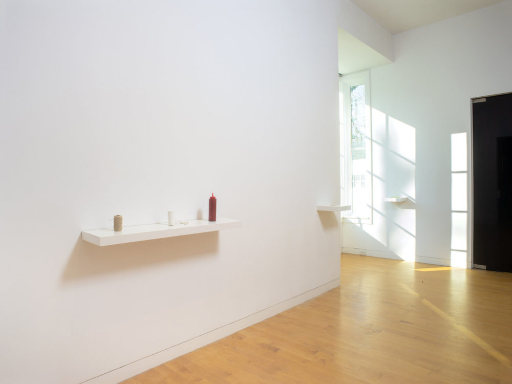 Three small objects sit on a white shelf in the gallery