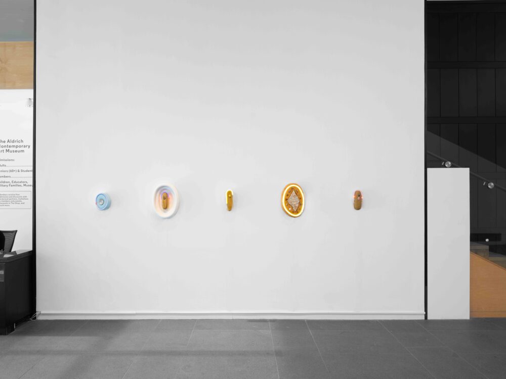 The wall of a museum lobby showcasing 5 circular artworks with bands of neon embedded with gemstones