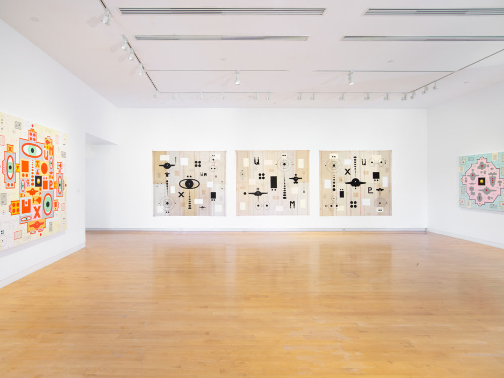 Three walls of a gallery with one painting hung on both the left and right walls and three paintings hung on the center wall.