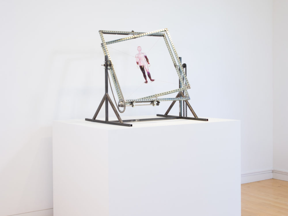 Kinetic sculpture with a metal frame that rotates a figure inside filled with red and blue liquids