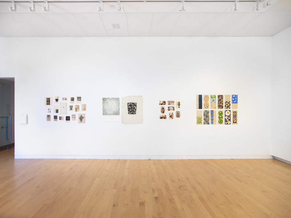 Groups of small works on paper in four clusters on a wall.