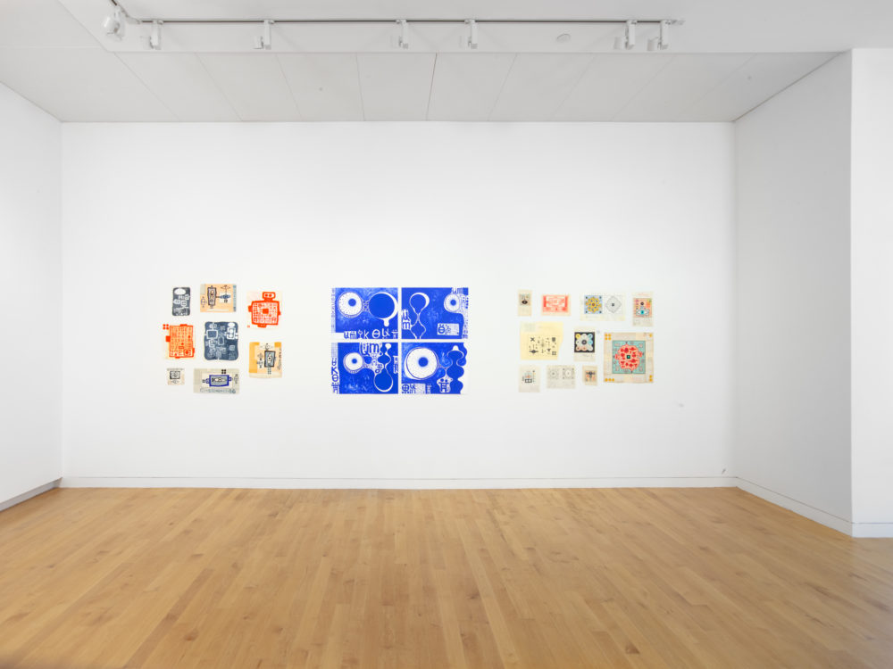 Three groups of works on paper on a wall.