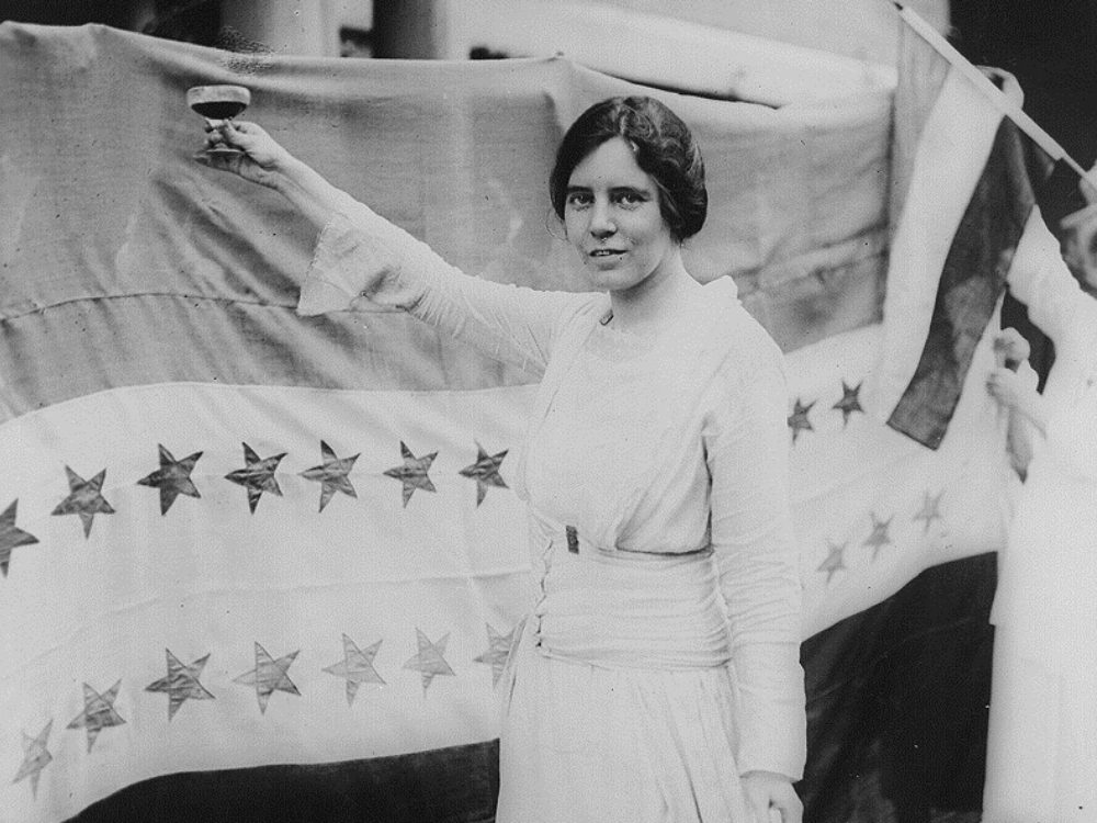 Person in white dress holds a flag with stars on it