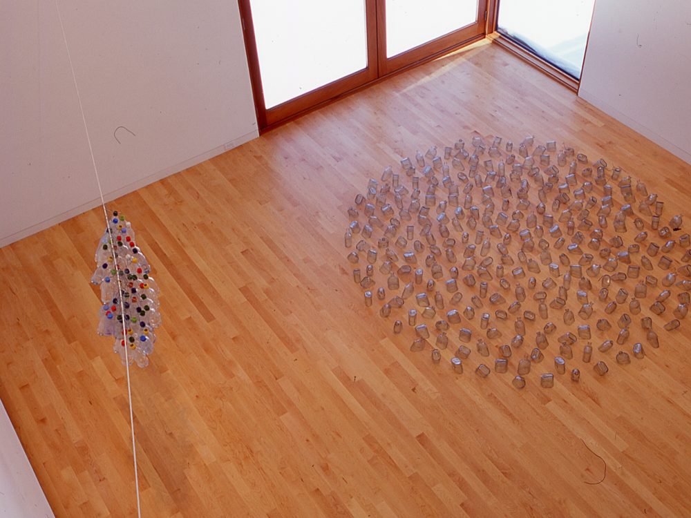 Left: plastic bottles hanging on white cord. Right: clear bottles arranged in large circle on wooden floor.