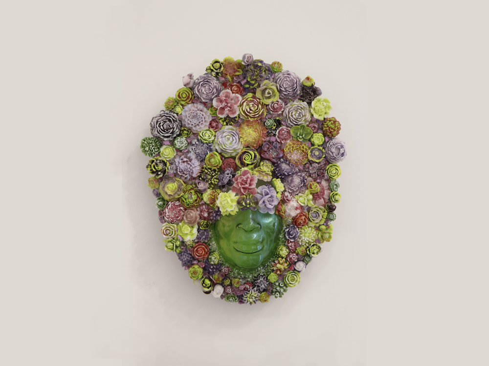 The bottom half of a face in transparent green glass surrounded by colorful glass flowers.