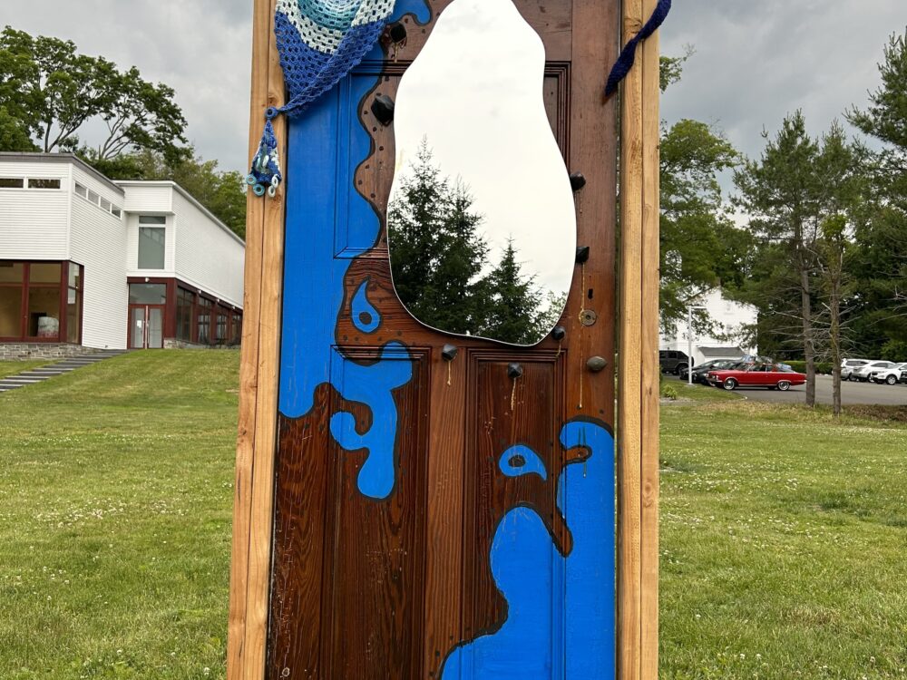 A painted door with a mirror on it in a wooden frame installed in the Museum's Sculpture Garden on the lawn.