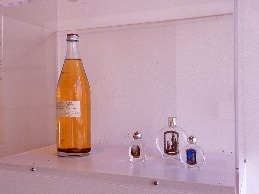 Left to Right: Tall bottle with amber liquid: three small perfume-like clear bottles with silver caps and religious iconography on front of each bottle.