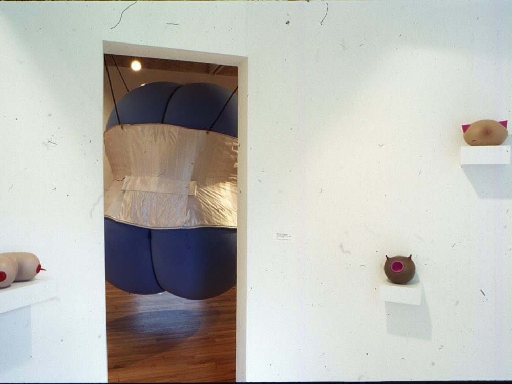 This is a photograph from the Pop Surrealism exhibition and you can see many small bodily sculptures with a large blue object in the doorway