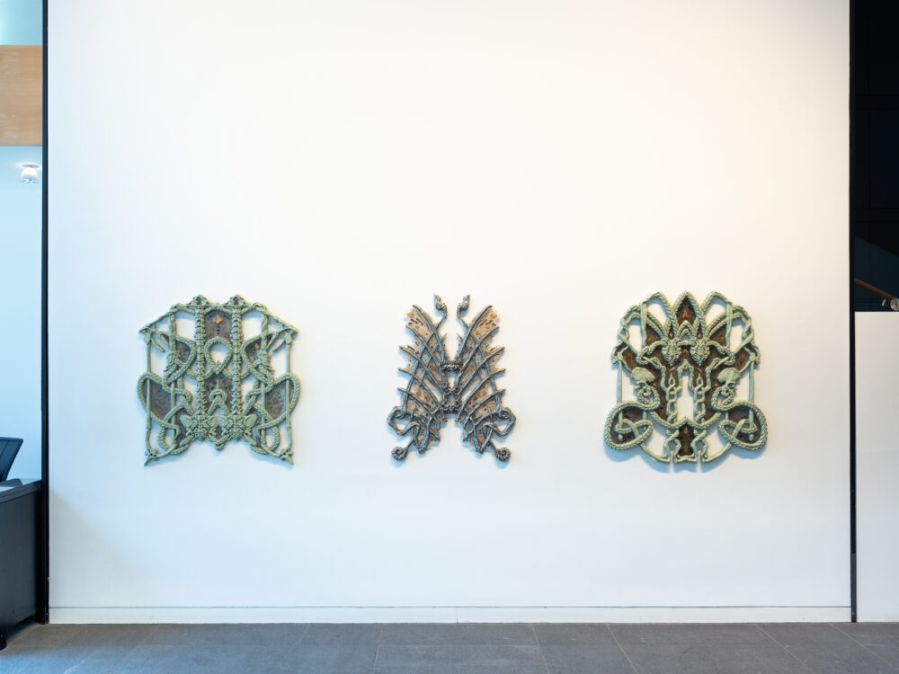 Three ceramic and resin sculptures hung on a white wall.